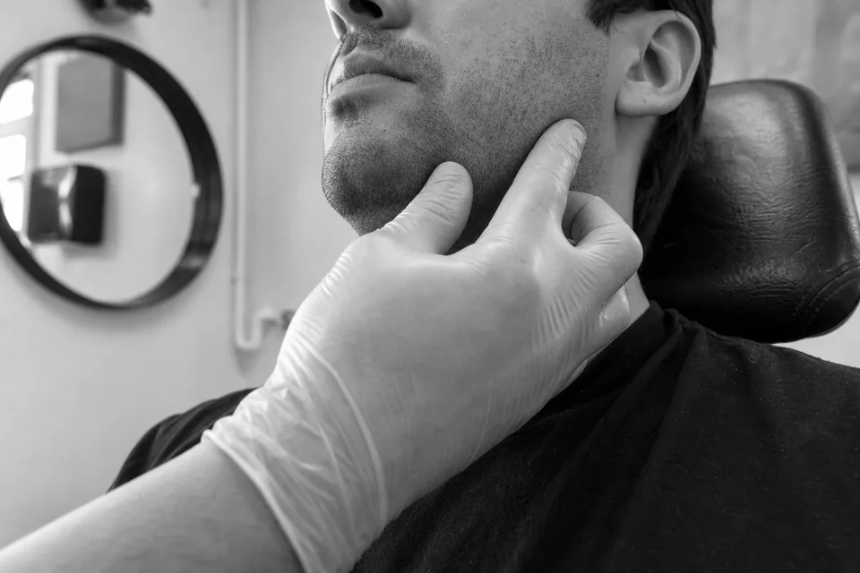 A provider in gloves palpating the jaw muscle of a client who clenches her teeth during a consultation