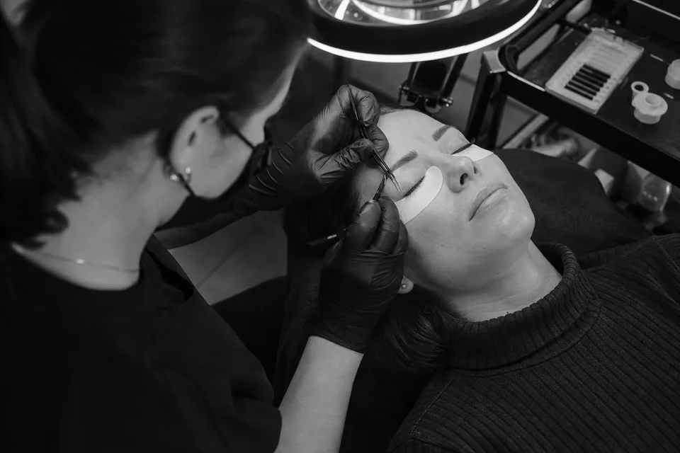 A lash artist with a magnifying lamp placing individual extensions on a reclined client