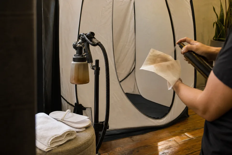 A spray tan booth with a pop-up tent, a spray gun on a stand and towels