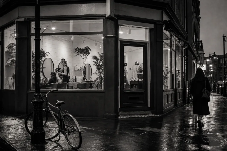 A small beauty studio storefront at dusk with lit windows on a quiet street corner