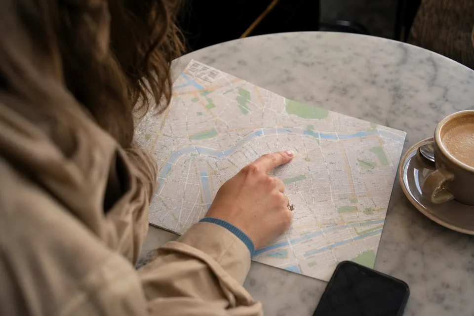 A paper street map of a city spread on a cafe table with a phone and a coffee cup