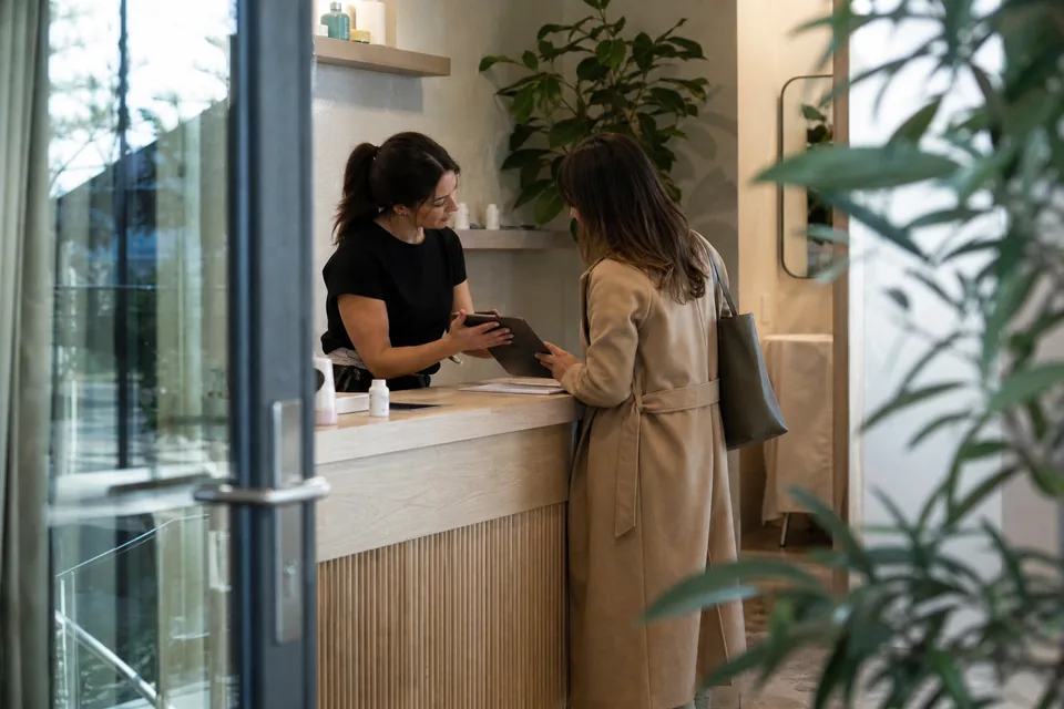 A client and a clinic receptionist looking at a tablet across a reception desk