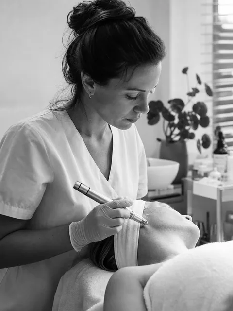 Esthetician holding a microneedling pen while a client rests with a headband on